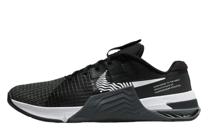 A pair of Nike Metcon 8 Gym athletic shoes featuring a black and gray color scheme with a distinctive textured design and brand logos.